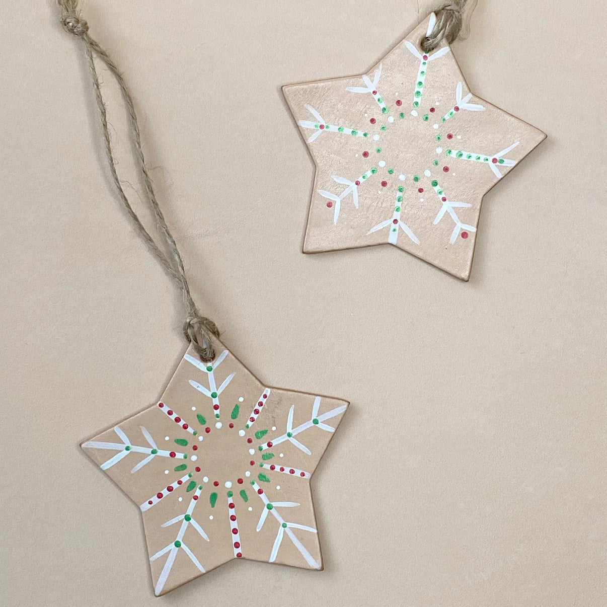 Two star-shaped decorations with painted patterns on a beige background. Artisan leather Christmas ornament with snowflake design and twine hanging loop.