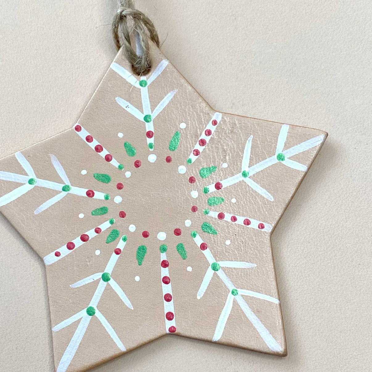 Star-shaped decorative ornament with white, red, and green patterns on a beige background. Personalised leather snowflake decoration with stamped initial. Made in Wales.