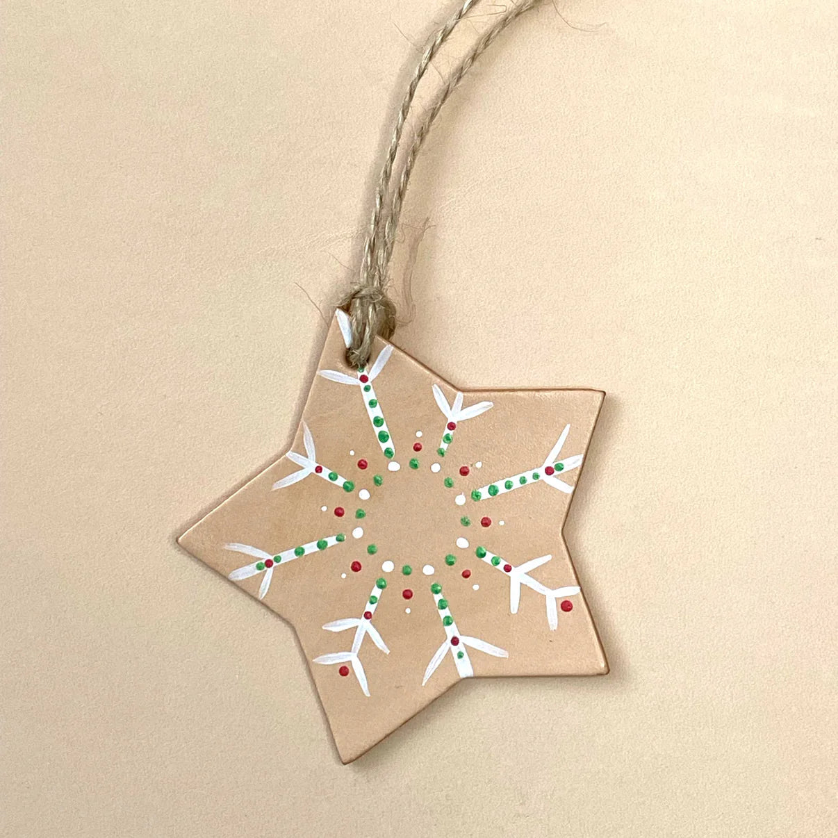 Star-shaped leather Christmas ornament with snowflake design on a beige background