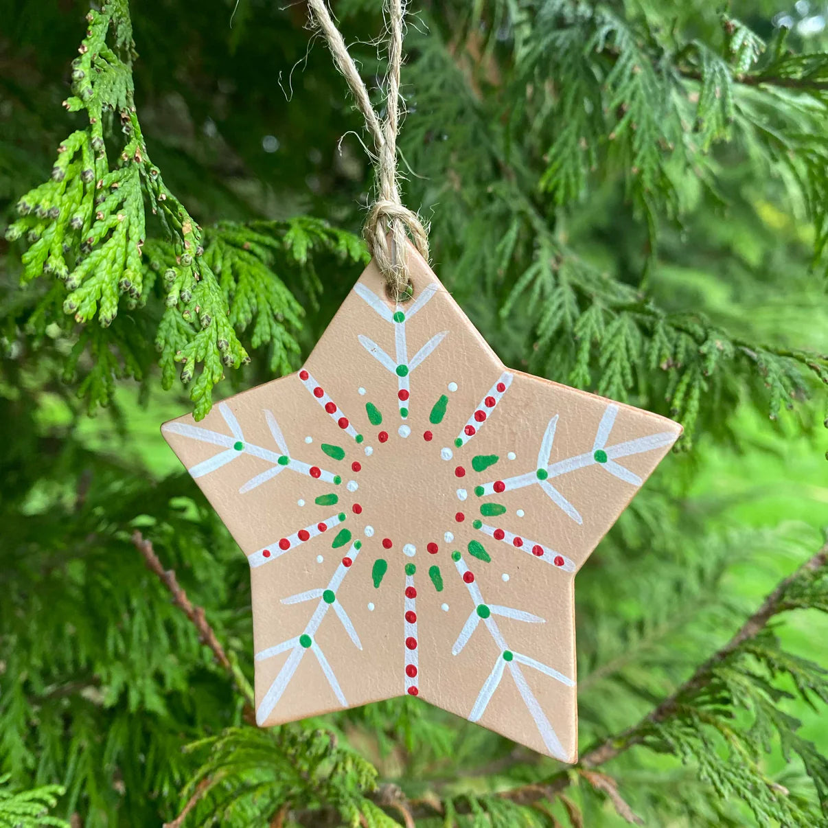 Star-shaped leather christmas ornament with red, green, and white patterns hanging on a tree branch, handmade by local maker in Wales.