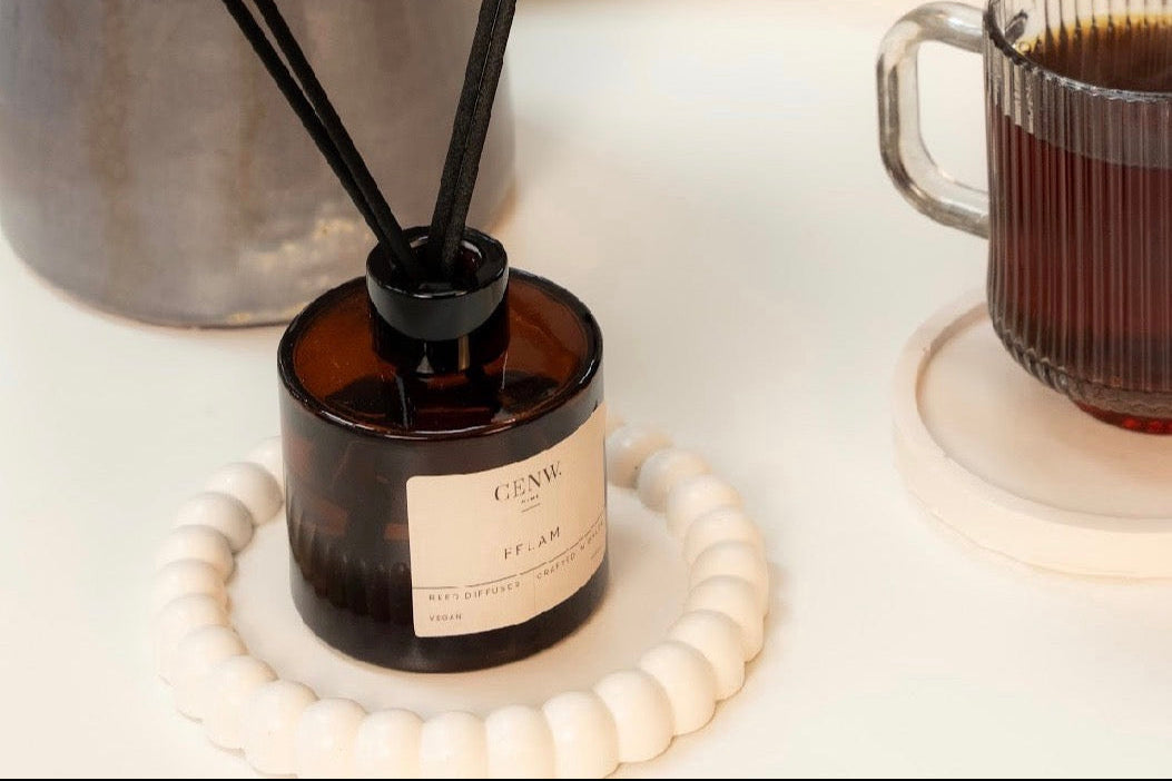 A diffuser with reeds on a table next to a mug of coffee and a vase. 100ml made in Wales with natural fragrance oils.