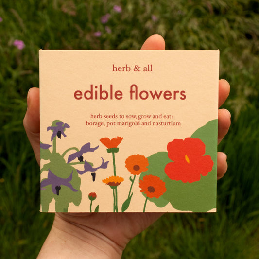Card with 'edible flowers' text and floral illustrations held in front of a grassy background