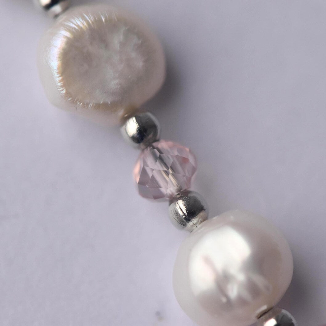 Close-up of a pearl necklace with silver and pink beads on a light grey background, handmade in Wales