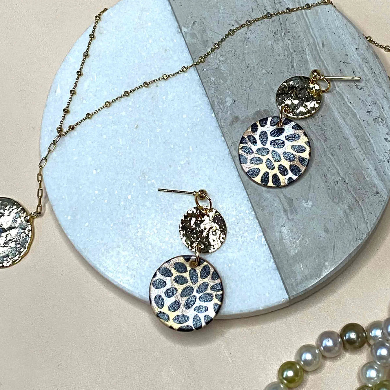 Earrings set and a necklace on a stone surface. Wild Petal hand-painted leather gold drop earrings handmade in the UK