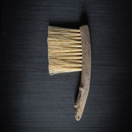 Eco friendly wooden cleaning brush handmade in Wales, with wooden handle and bristles on a dark textured surface. 