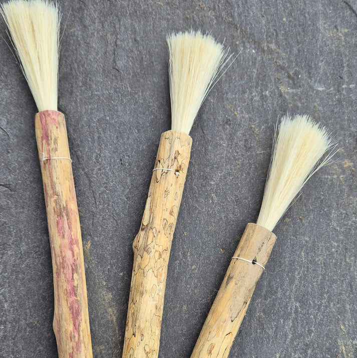 Three wooden brushes with bristle heads on a dark surface. Handcrafted driftwood paintbrush for expressive art techniques