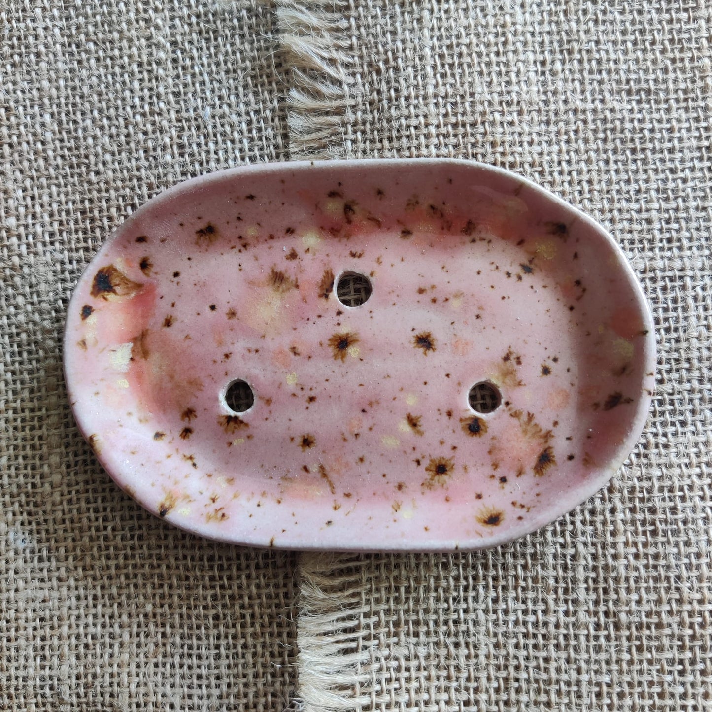 Peach coloured ceramic soap dish with speckled pattern on a textured fabric background. Handmade in Wales.