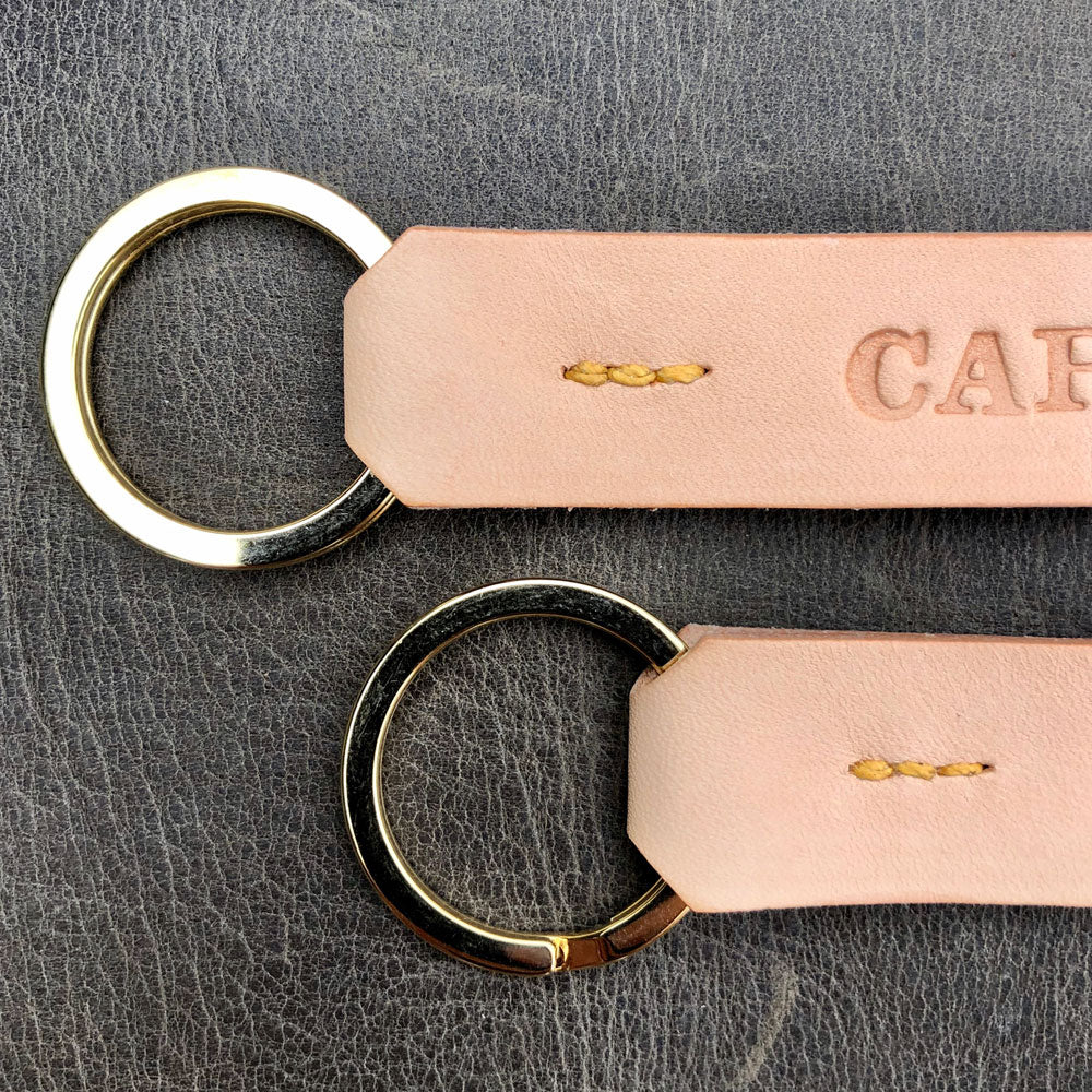 Two leather keychains with gold rings on a textured gray surface. houghtful Welsh housewarming gift supporting small business