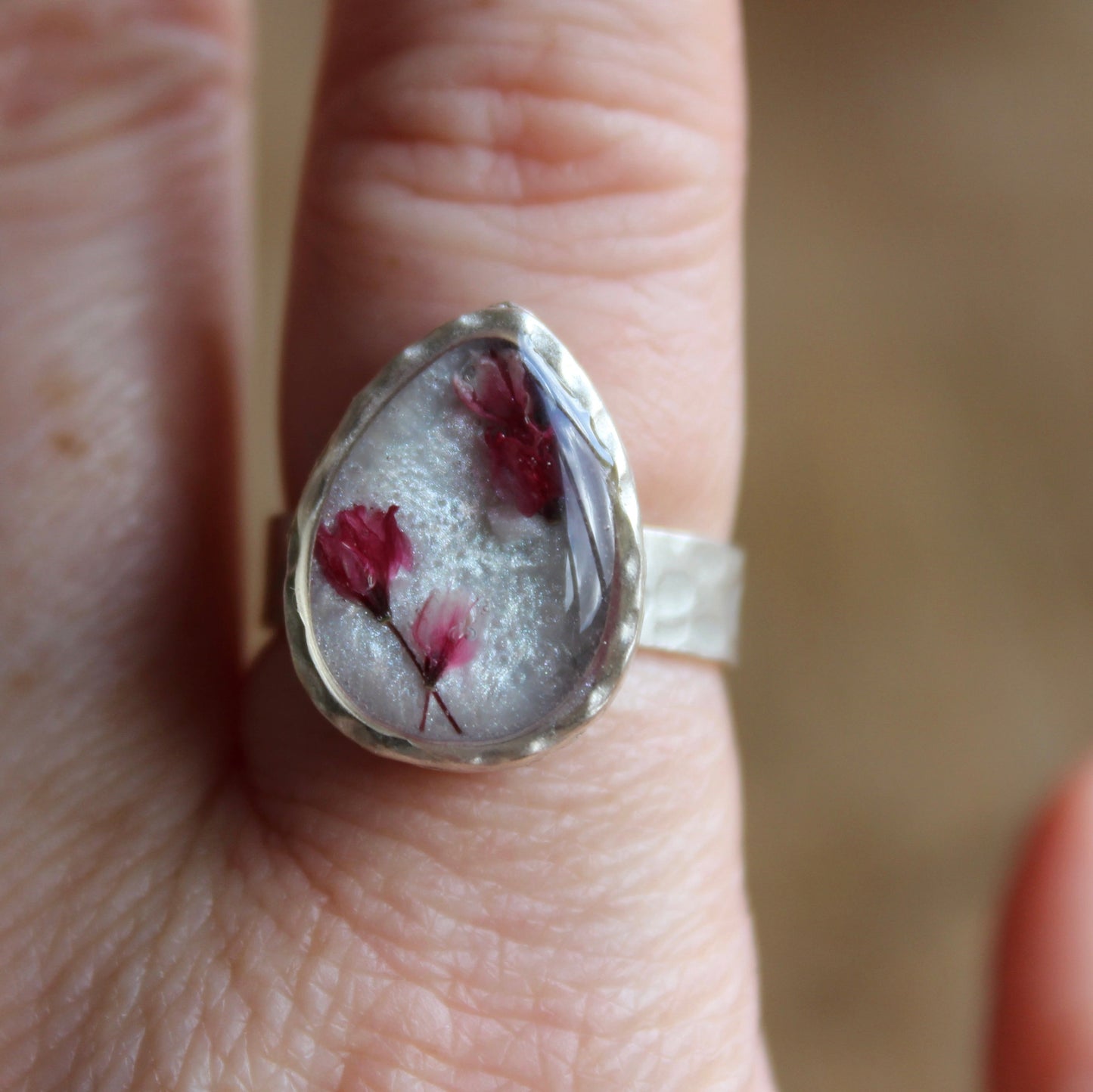 Silver ring with embedded dried flowers on a finger against a blurred background. Made in Wales.